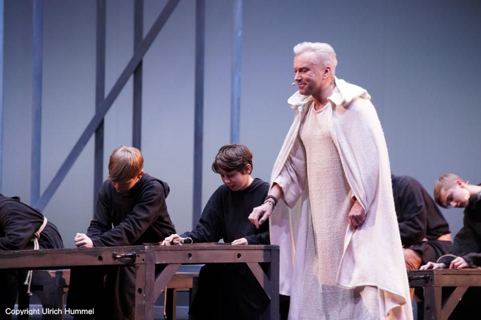 An der Schule unterrichtet Aeskulapius die Kinder. Mit ruhiger Strenge korrigiert er Fehler, nur die untadelige Arbeit Johannas findet seine volle Anerkennung. paepstin musical stuttgart 034